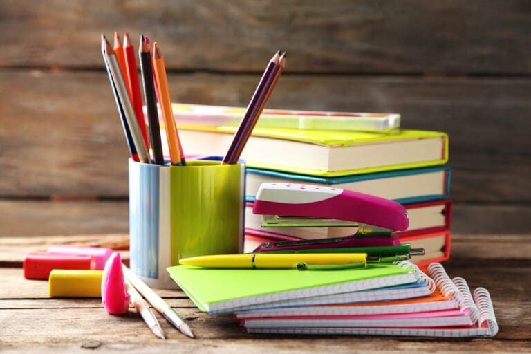 A stack of books, a cup full of pencils and a stack of notebooks on a table.